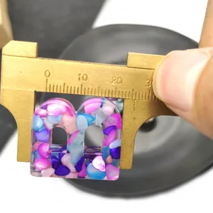 Macro view of 23mm resin alphabet charm with colorful stone inlay being measured by caliper
