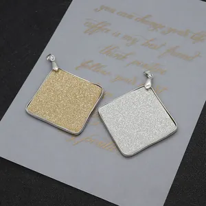 Détail de pendentifs carrés de 53mm en or et argent avec une texture pailletée fine