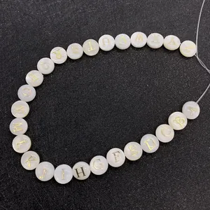 Macro shot of 26 round natural white shell alphabet beads with gold engraved letters