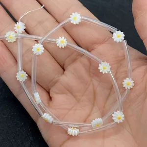 Macro view of white shell daisy beads with yellow centers held in hand for size reference