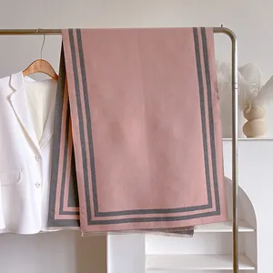 Detail of pink cashmere scarf with grey stripes, fringe edges, and soft knit texture