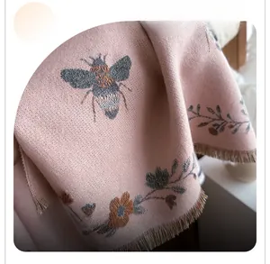 Close-up of pink knit scarf featuring bee floral embroidery and elegant long tassels