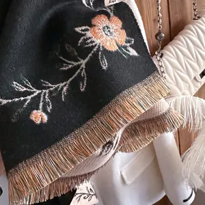 Detailed embroidery of orange floral patterns and golden tassels on black cashmere shawl