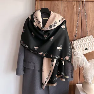Detail of floral and bee jacquard pattern on a dual-tone cashmere-like tassel shawl