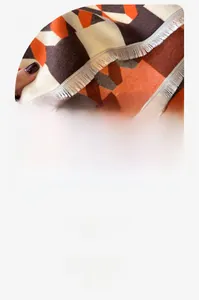 Close-up of cashmere-feel scarf texture with orange geometric patterns and fringe detail
