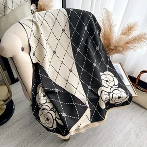 Detail of camellia floral knit shawl with fringes and diamond grid pattern on sofa