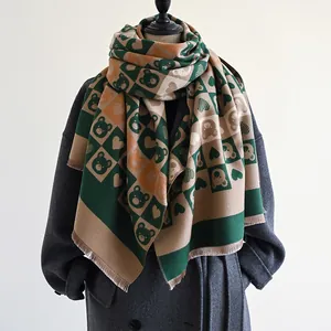 Détail de l'écharpe épaisse à carreaux avec motif ours et franges sur un manteau gris