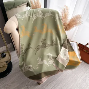 Close-up of thick sage green scarf with zebra pattern and fringed edges on sofa