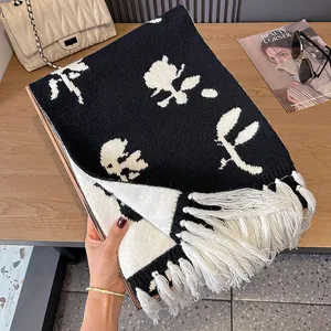 Close-up of black and white floral knit scarf with long tassels on a wooden surface