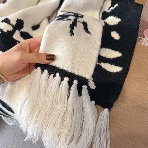 Detailed view of black and white knitted scarf with floral patterns and soft white tassels
