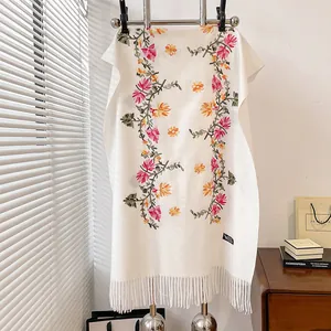 Detailed close-up of floral embroidery and fringe on a thick cream cashmere-feel shawl