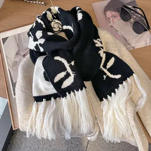 Thick black and white knit floral scarf with long tassels on a beige coat setting