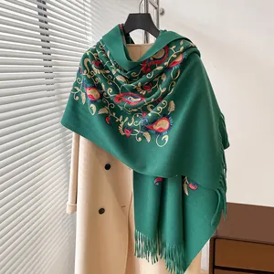 Dettaglio del ricamo paisley verde e frange su scialle in cashmere sopra un cappotto