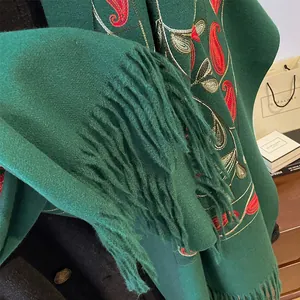 Détail de la broderie paisley ethnique et des franges sur l'écharpe vert foncé