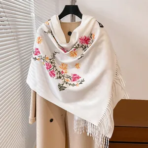 Detailed close-up of white cashmere-like scarf with colorful floral embroidery and fringe