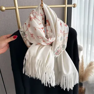 Close-up of floral embroidery on a white cashmere-like pashmina scarf with fringe detail