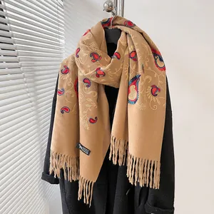 Dettaglio macro della sciarpa in cashmere beige con ricami paisley rossi e frange