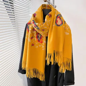 Dettaglio di sciarpa pashmina gialla con ricamo paisley e frange su cappotto nero
