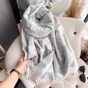 Luxurious camellia jacquard cashmere scarf with fringes draped on a beige velvet chair
