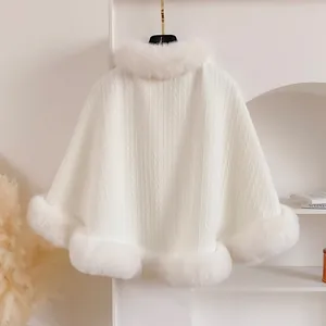 Detailed view of white knitted cape featuring plush faux fur collar and textured fabric