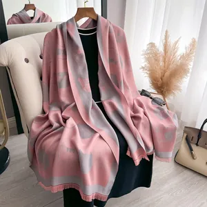 Close-up of pink and grey scarf with cat print and tassels on a wooden hanger