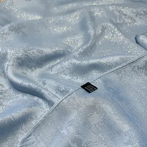 Close-up of light blue silk scarf fabric with shimmering texture and fringe edges