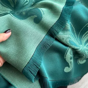 Détail de l'écharpe en jacquard vert foncé avec motifs floraux et pompons à franges
