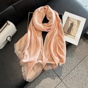 Peach pink silk-like scarf with camellia jacquard and frayed edges on a leather bench
