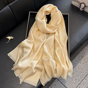 Detail of champagne gold silk scarf with jacquard pattern and tassel edges on a black tray
