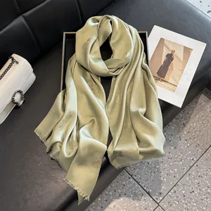Elegant grass green satin scarf with floral patterns and tassels on a black leather tray