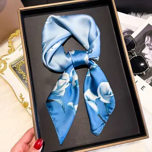 Close-up of sky blue silk scarf with white floral patterns in a black luxury gift box