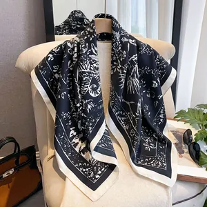 Detail of silk-like square scarf with black floral print draped on a wooden hanger