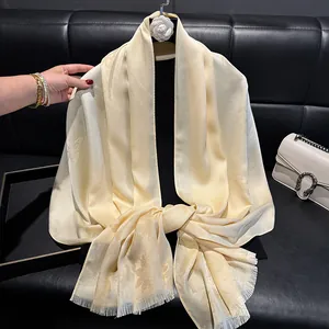 Detail of champagne butterfly jacquard silk scarf with fine fringe on a black surface