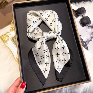 Flat lay of a 70cm silk scarf with black floral prints on cream base and styled props