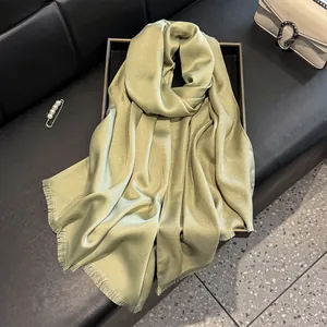 Detail of light green silk scarf with subtle shimmer finish and fringe edges in a gift box