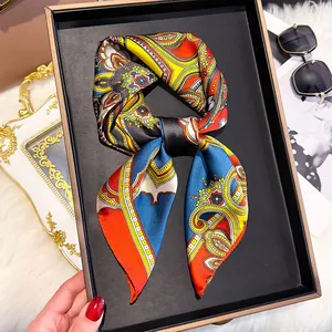 Detailed close-up of a paisley printed silk square scarf tied in a bow inside a gift box