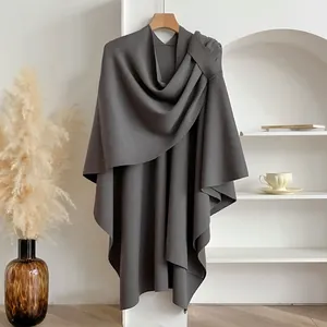 Detail of dark grey knitted poncho with elegant shoulder knot on a wooden hanger