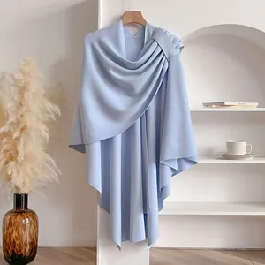 Detail of light blue knitted poncho with buckle closure on a minimalist background