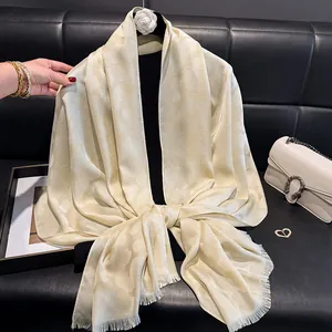 Detalle de bufanda de seda crema con patrón jacquard, borlas y adorno de flor de camelia
