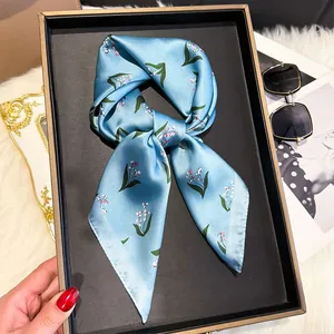 Detail of silk-like square scarf featuring lily of the valley print tied in a bow