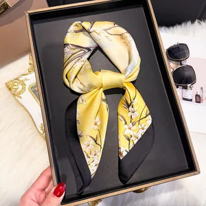Detail of yellow silk scarf with white flowers and black border tied in a bow