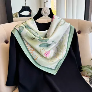 Détail d'un foulard en soie de 90 cm avec imprimé floral vert sur un pull noir