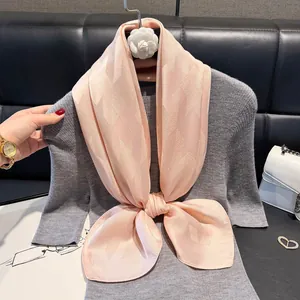 Detail view of pink houndstooth silk scarf tied in a bow on a grey knitted top