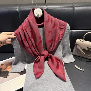 Dettaglio di un foulard in seta jacquard rosso annodato su un maglione grigio su fondo pelle