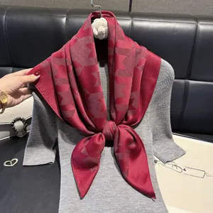 Detail of burgundy silk scarf featuring geometric M-pattern over grey knitwear