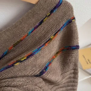 Close-up of brown knit poncho texture featuring colorful rainbow stripes and tassel details