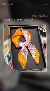 Close-up of orange silk scarf with floral patterns on a black tray with sunglasses