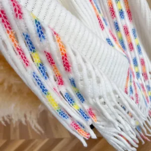 Nahaufnahme eines weißen Strickponchos mit bunten Regenbogen-Quasten und Textur