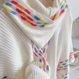 Nahaufnahme des weißen Strickponchos mit weicher Textur und lebhaften Regenbogen-Streifenkanten