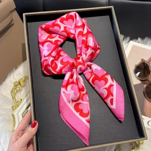 Close-up of heart print silk square scarf tied in a bow on a black textured tray